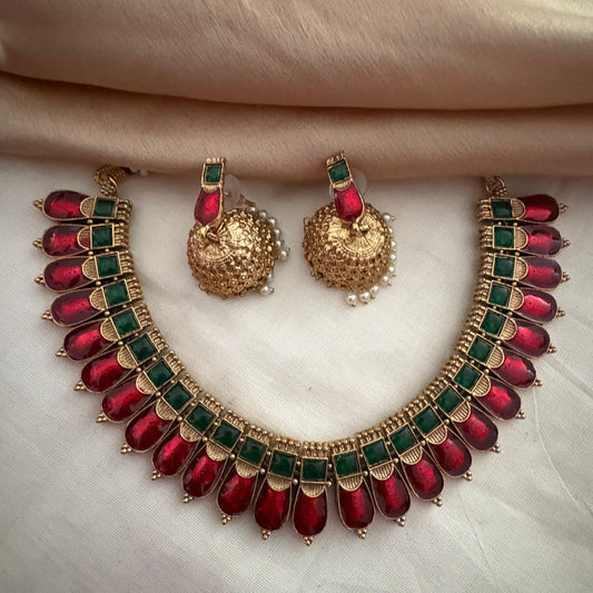 Gold necklace with red and green stones and matching earrings on a light fabric background